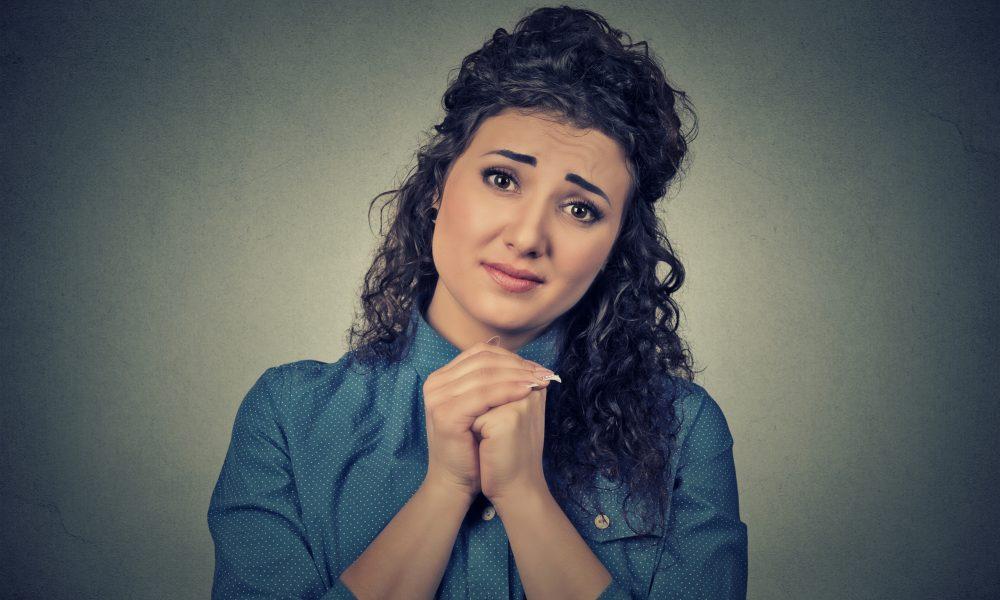 young woman gesturing with clasped hands, please forgive me